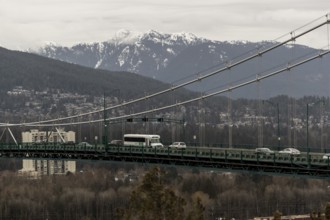 Suspension bridge with traffic, framed by an urban cityscape and mountain backdrop in Vancouver,