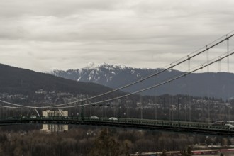 Suspension bridge spanning a city and mountainous landscape under cloudy skies in Vancouver,