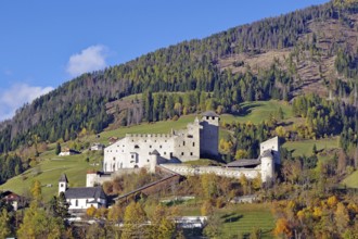 Historic mountain castle above an autumnal valley, small church in front of it, clear sky,