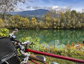 View over the handlebar of a shimmering green river in front of autumn trees and mountains, bicycle