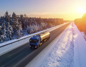 Petrol cargo truck lorry tanker driving on highway hauling oil products at sunrise, wide snowy