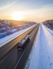 Petrol cargo truck lorry tanker driving on highway hauling oil products at sunrise, wide snowy