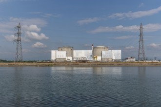 A large industrial nuclear power plant is located on a quiet water front. Two tall cylindrical