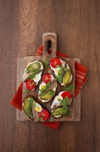 Sandwiches on rye bread with sprats, quail eggs, fresh tomatoes and pickled cucumber, on a wooden