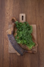 Fresh cilantro and dill are placed on a wooden cutting board next to a machete. The herbs are