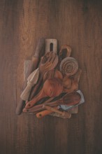 A variety of wooden kitchen utensils are arranged on a dark brown wooden surface. Items include