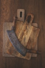 A large curved knife rests on top of two wooden cutting boards on a rustic surface. The knife shows