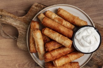 Fried spring rolls with cheese, on a wooden background, with cream sauce, no people