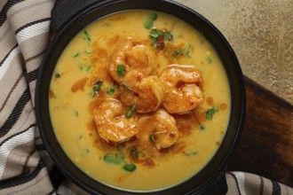 Creamy shrimp curry with spices, garnished with herbs, on a textured background, homemade, no