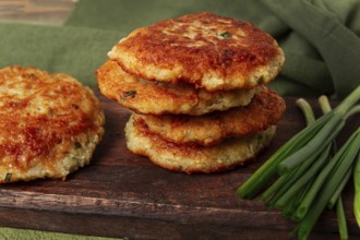 Crispy potato pancakes Latkes, stacked on a wooden board next to fresh green onions, natural light,