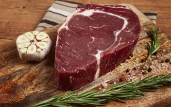 Raw steak, beef steak, rib eye steak, on a cutting board, freshly frozen, with spices and herbs, on
