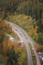 Road and railway line lead through autumn-colored forest, with construction machinery along the