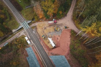 Construction site next to railway line with excavators and trucks surrounded by autumn forests,