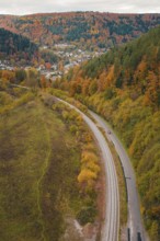 Road and rail along an autumnal hill surrounded by forest, Hermann-Hesse-Bahn construction site,