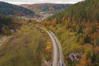 Winding road with rails through autumnal forest, village in the background, Hermann-Hesse-Bahn