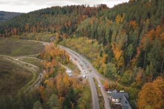 Road next to railroad tracks through autumnal forest and hills, Hermann-Hesse-Bahn construction