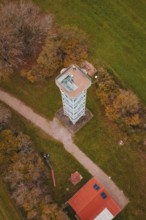 Aerial view of a tower surrounded by trees and paths in autumn colors and green fields,