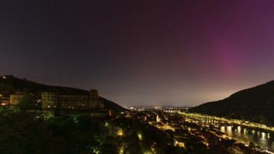 Nocturnal sky with aurora borealis over Heidelberg. Heidelberg Castle on the left, the Neckar river