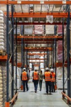 Logistics team walking down a wide warehouse aisle between tall pallet racks, inspecting inventory