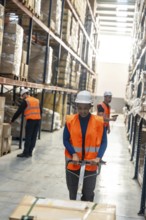 Diverse logistics team preparing packages and moving products on pallet jacks inside a modern