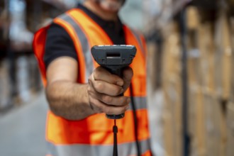 Warehouse worker wearing a safety vest using a barcode scanner to manage inventory and streamline
