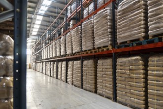 Spacious industrial warehouse aisle with pallets of identical sacks stacked on tall metal shelving,