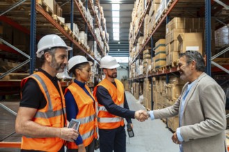 Logistics manager smiling and shaking hands with a warehouse worker in safety gear, celebrating a