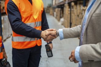 Two people, one wearing a safety vest and scanner, the other in a business suit, shaking hands in a