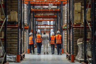 Group of diverse warehouse workers in safety vests and a manager inspecting inventory and racks,
