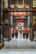 Group of diverse workers and a manager in safety vests and hard hats walking down a long aisle