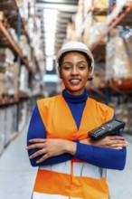 African american woman worker wearing a safety vest and hard hat, holding a portable scanner,