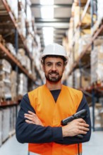 Warehouse worker in safety vest and hard hat smiles at camera while holding a barcode scanner in a
