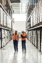 Warehouse workers in high visibility vests and hard hats checking inventory and managing logistics