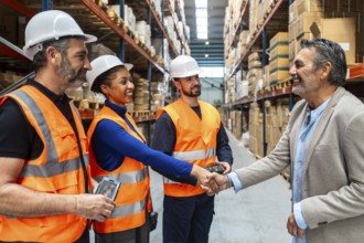 Business executive is shaking hands with a diverse team of warehouse workers wearing safety vests