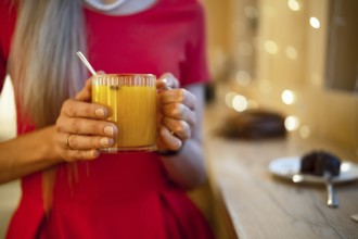 A woman in a bright red dress holds a glass of warm orange drink, enjoying a relaxing moment. Soft