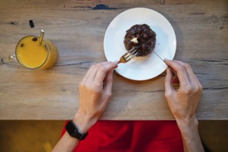 A person sits at a wooden table, ready to enjoy a delicious dessert. A fork is poised over the