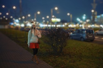 A woman walks along a city street at night, wearing a warm outfit that includes a short coat,