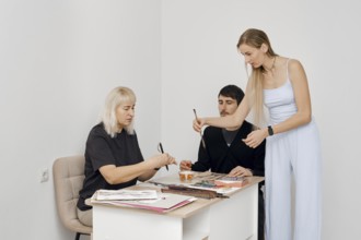 Three individuals engage in a creative workshop, sharing art supplies and discussing their work.