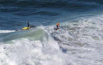 Surfers with their jet ski pilots in the Atlantic waves below Farol de Nazaré, Forte São Miguel,