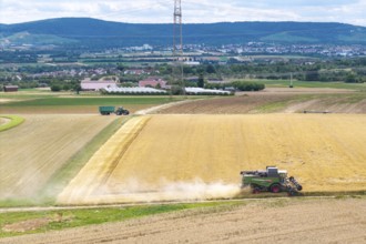Harvester works in vast fields, clear view of adjacent landscape due to sunny weather, Mähresc Korb