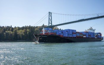 Container ship loaded with containers sails under the Lions Gate Bridge, Vancouver Harbor,