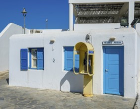 Mykonos, Cyclades, Greece - Old yellow telephone box in front of white house with blue shutters in