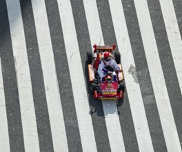 People in costumes drive small go-kart racing cars across zebra crossings, Shibuya Crossing,