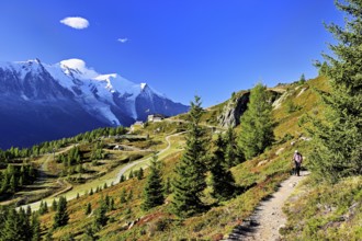 Female hiker on a hiking trail with the La Flégère cable car mountain station and the snow-covered