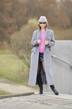 A woman showcases striking urban fashion by wearing a bright pink sweater, a long gray coat, and