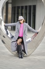 A woman poses confidently in an urban environment, showcasing vibrant clothing against contemporary