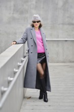 A stylish model poses confidently in an urban setting, wearing a vibrant pink sweater under a gray