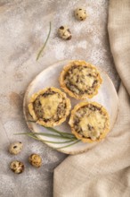 Tartlets with meat and cheese on brown concrete background and linen textile. top view, flat lay,