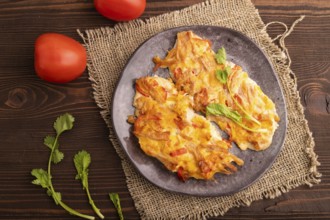 Baked chicken meat with cheese and tomatoes on brown wooden background and linen textile. top view,