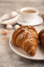 Croissant on white plate on brown concrete background and linen textile, cup of coffee, side view,
